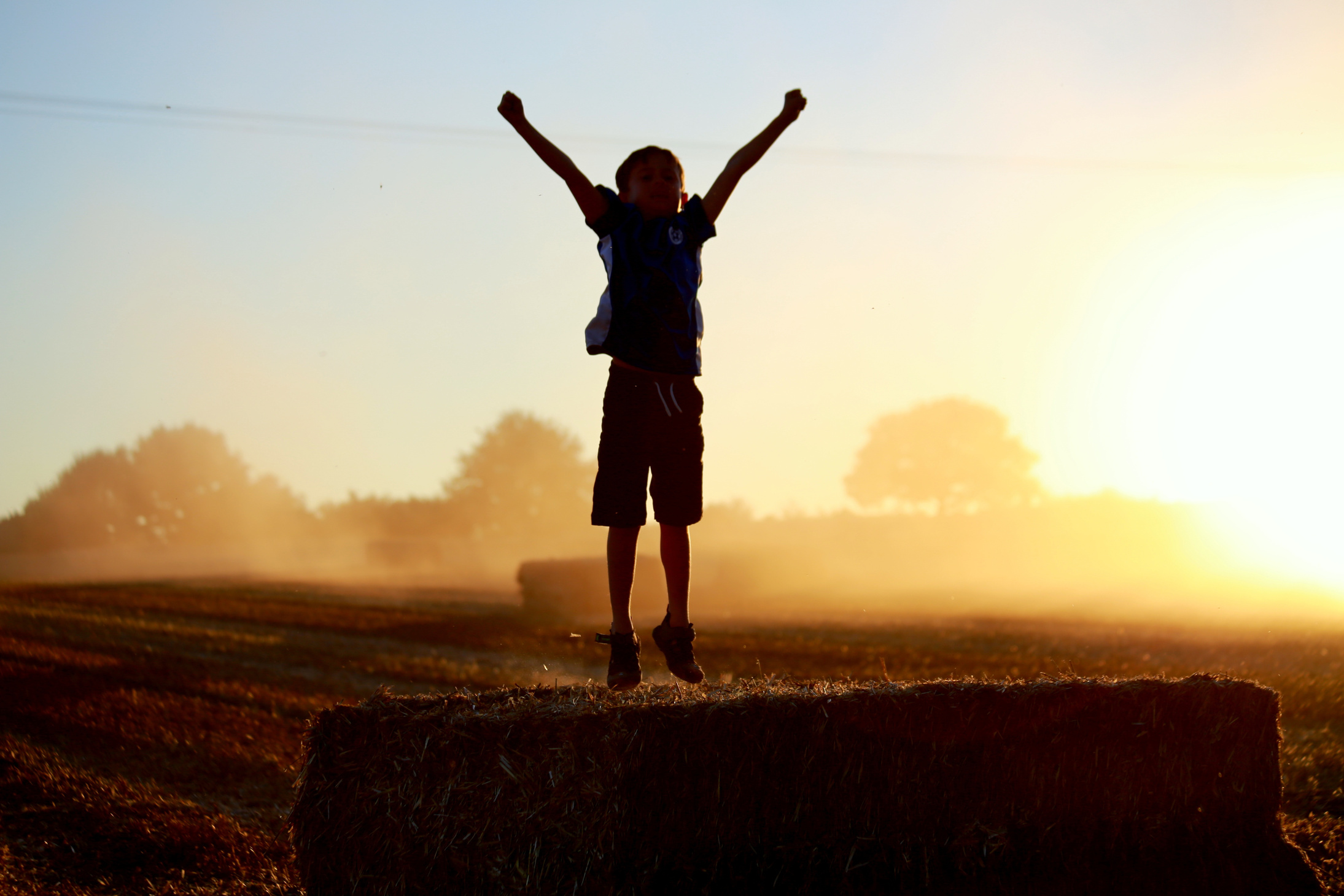Little Boy Jumping in the Field at Sunset