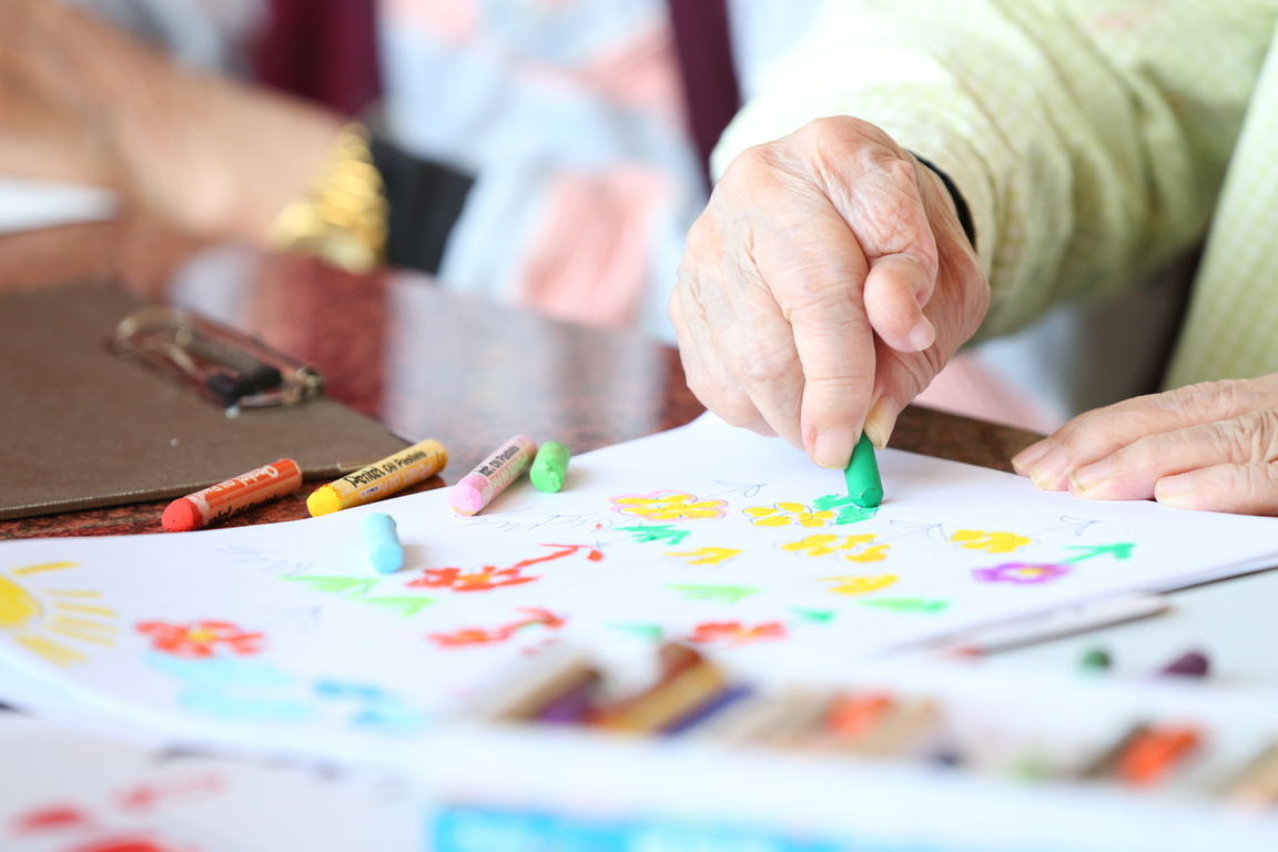 Crop senior person drawing with crayons